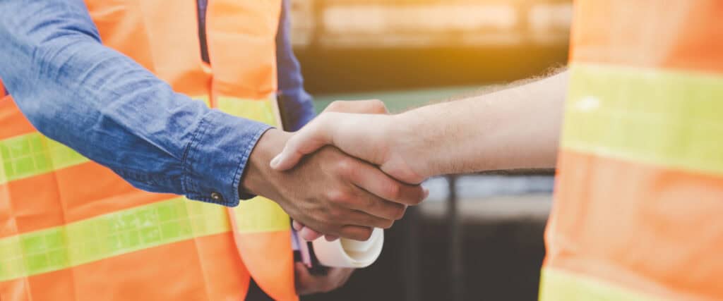 Two workers in high-vis shaking hands, highlighting collaborative action for PFAS elimination Australia between government and industry.